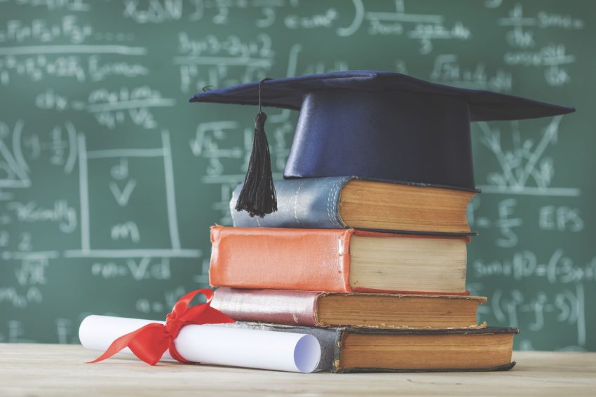 A stack of books topped with a graduation cap