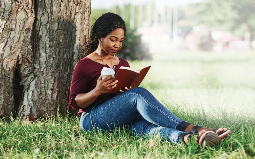 Woman reading under a tree while enjoying a cup of coffee