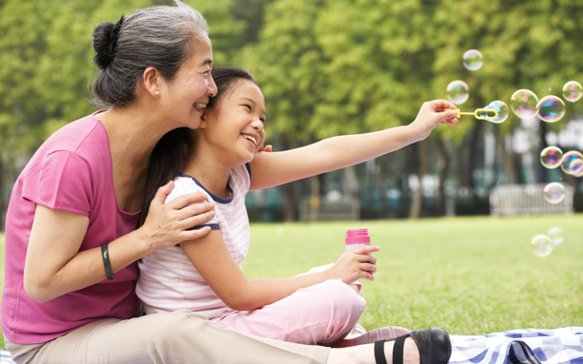 Grandmother and granddaughter blowing bubbles in the park