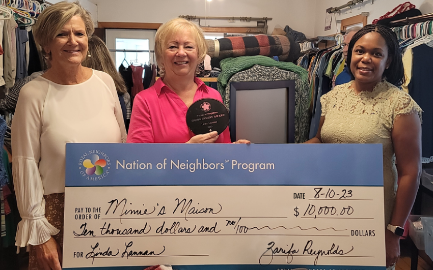 Three happy women with a giant check for $10,000 inside of a clothing shop. The middle one is holding a black circular award.