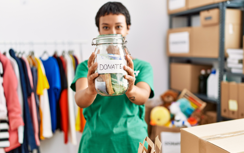 Person holding a donate jar with clothing, toys, and donations in boxes behind them.